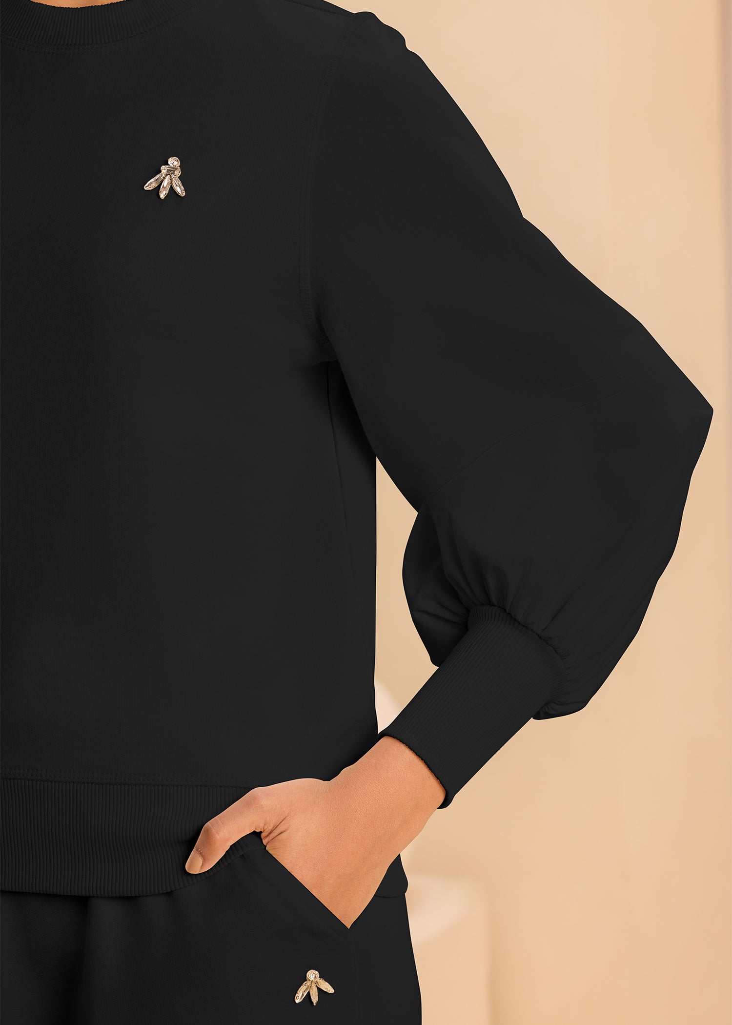 A cozy black sweatshirt adorned with a bold rhinestone emblem at the corner, ideal for a trendy look.