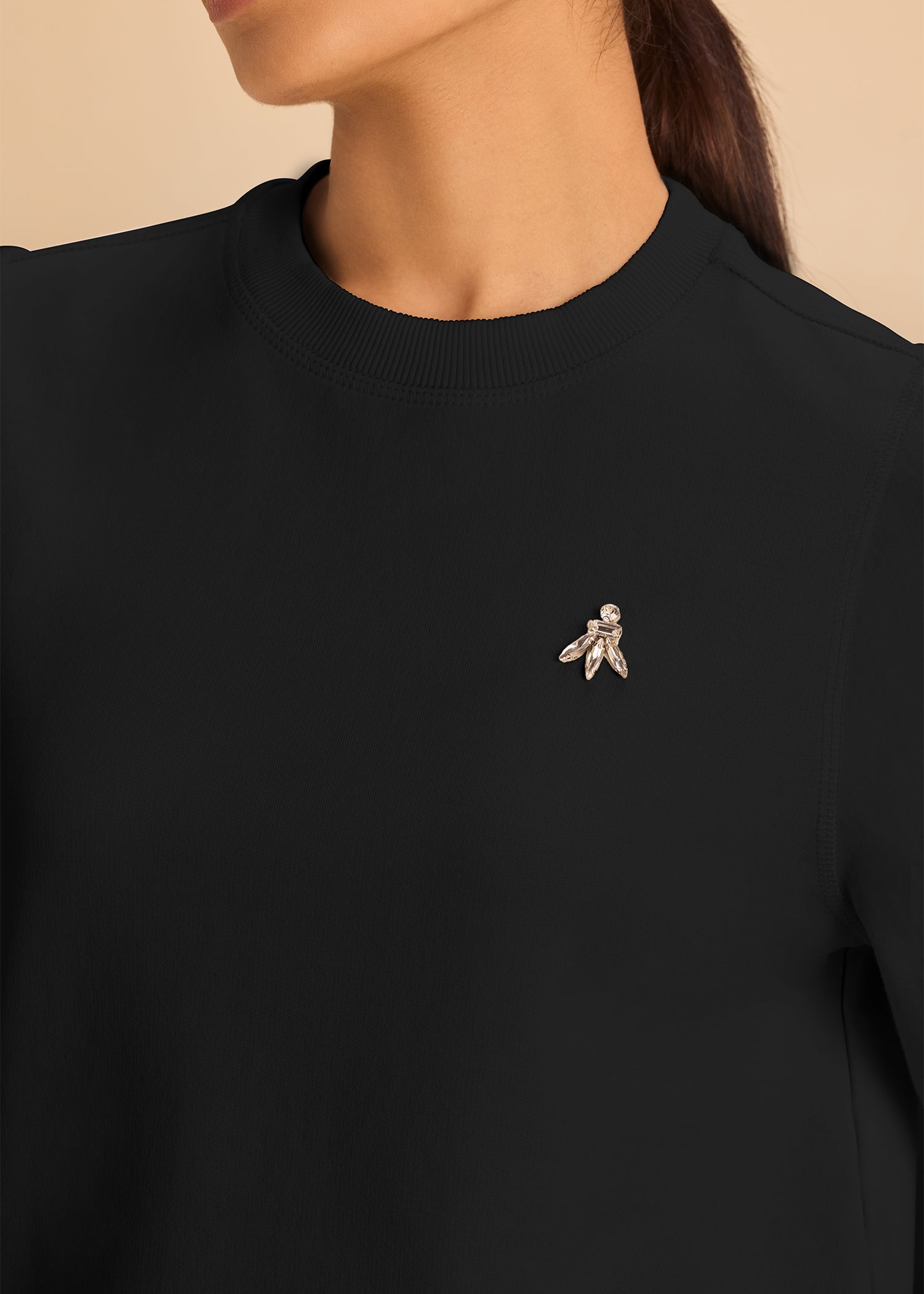 Partial view of a woman wearing a black top adorned with a decorative brooch featuring a leaf design. The brooch is pinned near the collar. 